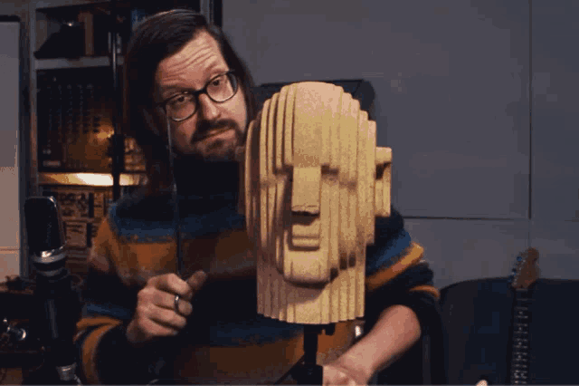 a man wearing glasses is holding a sculpture of a face
