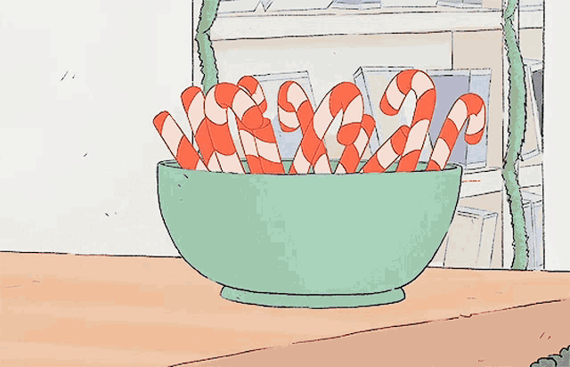 a green bowl filled with red and white candy canes on a table