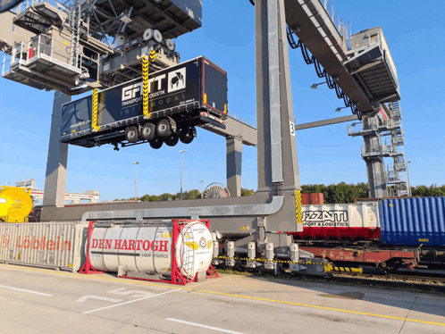 a container with den hartogh written on it is being lifted by a crane