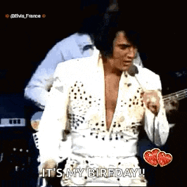 elvis presley is standing on stage holding a microphone and singing into it .