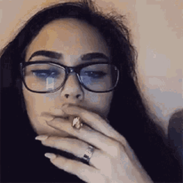 a woman wearing glasses is smoking a cigarette while wearing a ring on her finger .