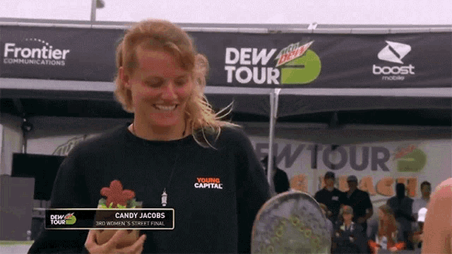 candy jacobs is holding a snowboard in front of a dew tour sign