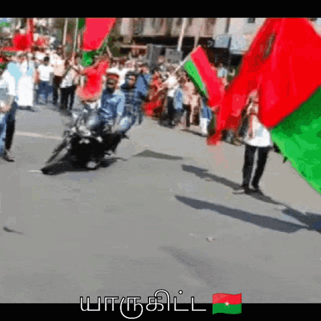 a man riding a motorcycle with a green and red flag in front of a crowd of people
