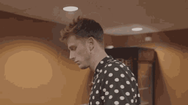 a young man wearing a black and white polka dot shirt is looking at the camera .