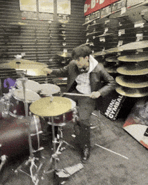 a man is playing drums in a store with a sign that says ' original cymbals ' on it