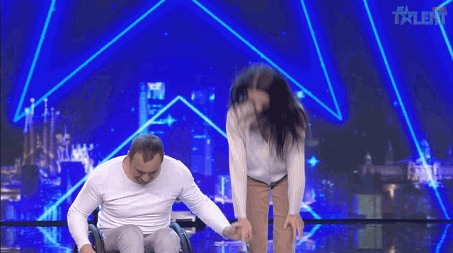 a man in a wheelchair is holding a woman 's hand on a stage with the word talent on the bottom right