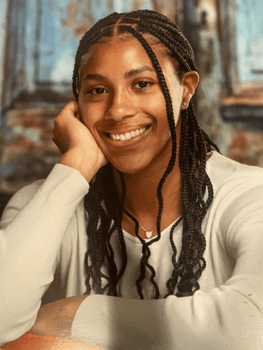 a girl with braids is smiling with her hand on her face