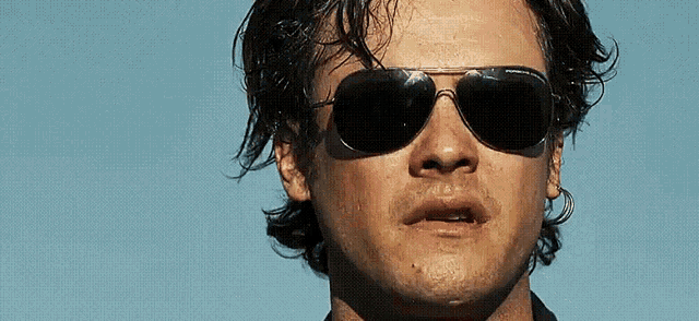 a close up of a man wearing sunglasses pointing at something