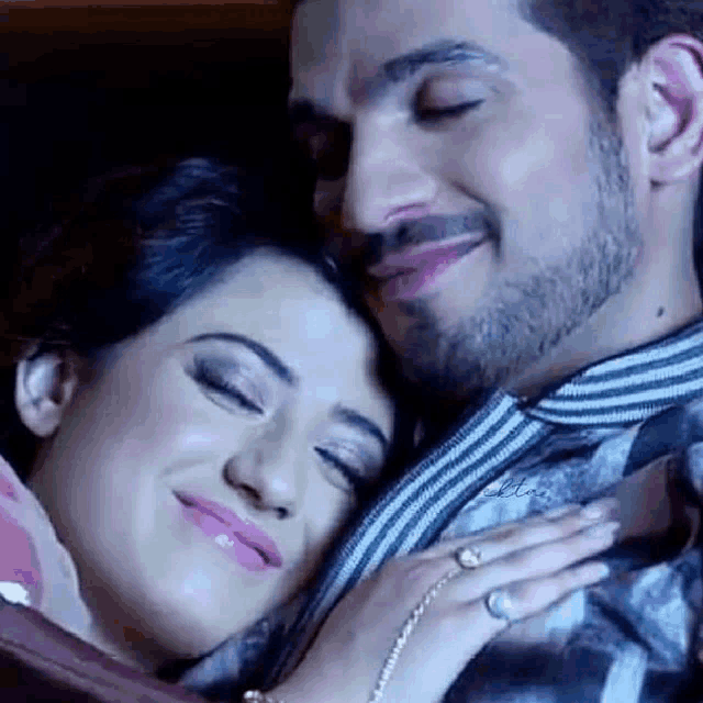 a man and a woman are hugging each other with their eyes closed and smiling .