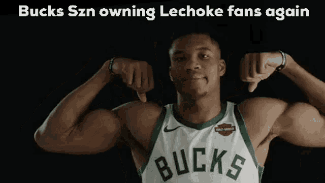 a basketball player in a bucks jersey is flexing his muscles and giving a thumbs down .