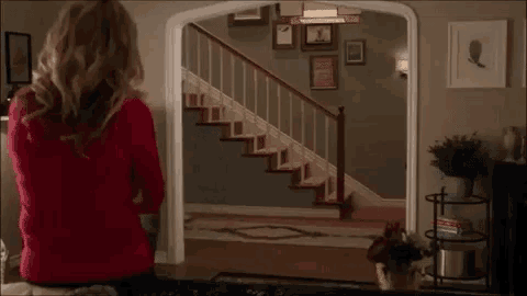 a woman in a red sweater is standing in front of a doorway looking at a man in a chef costume .