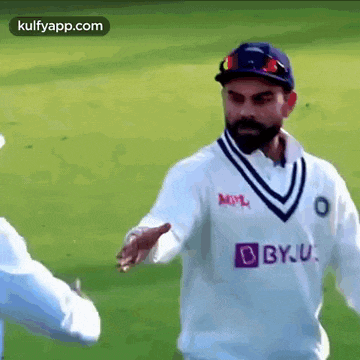 a cricket player in a white shirt is shaking hands with another player .