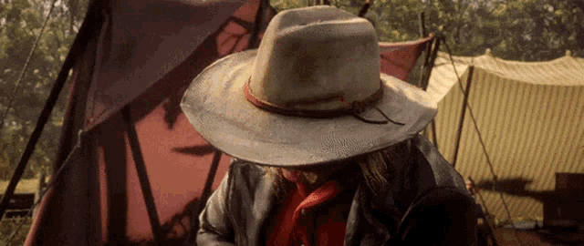 a man wearing a cowboy hat and a red shirt is standing in front of a tent .