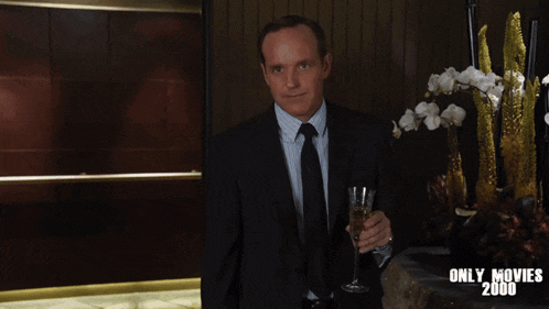 a man in a suit and tie is holding a glass of wine in front of a sign that says " only movies 2000 "