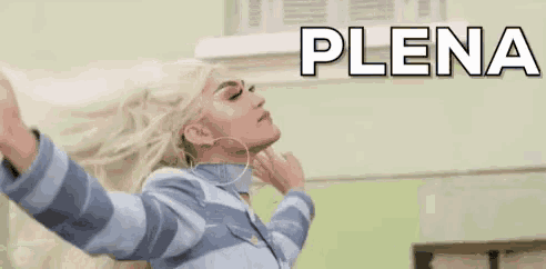 a woman with blonde hair is standing in front of a green wall with her arms outstretched and the word plena written above her .