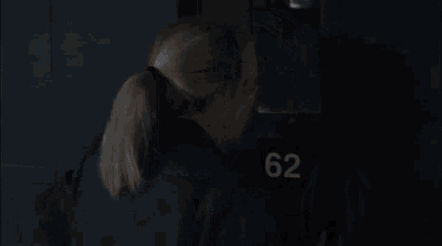 a woman in a dark room with the number 62 on the wall