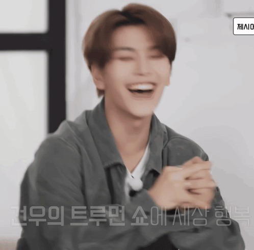 a man in a grey jacket is laughing with korean writing on the bottom right corner