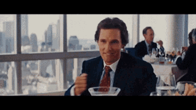 a man in a suit and tie sits at a table with a martini