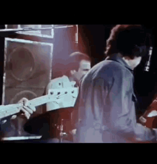 a man is playing a guitar on a stage while another man stands behind him .