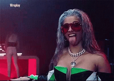 a woman with blue hair is sticking her tongue out while wearing sunglasses and a necklace .