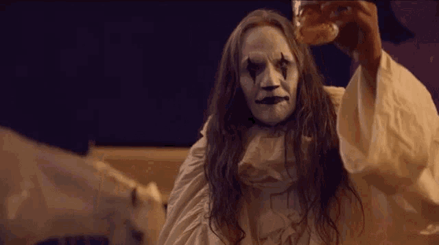 a woman with a clown makeup on her face is holding a glass of wine .