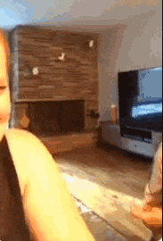 a woman is sitting in a living room with a fireplace and a television .