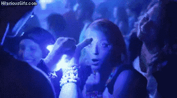 a group of people are dancing in a club with glow in the dark lights and a woman is pointing at her face .