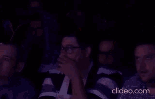 a group of people are sitting in a stadium watching a game and one man is raising his hand in the air .