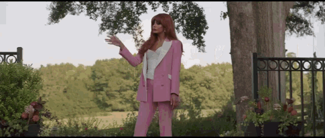 a woman in a pink suit stands next to a tree