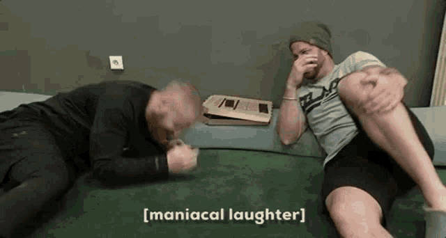 two men are laying on the floor laughing and one of them is covering his nose .