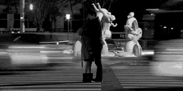 a man and a woman are kissing on a crosswalk in front of a statue .