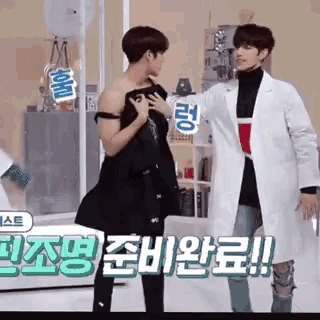 two men are standing next to each other in a room and one of them is holding another man 's shirt .