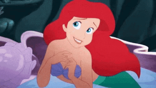 ariel from the little mermaid is smiling and looking at the camera while swimming in the ocean .