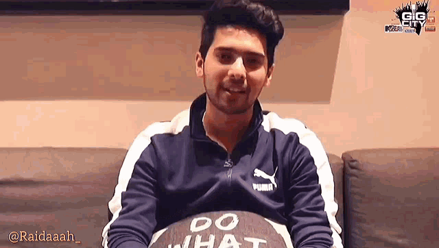 a man wearing a puma jacket is sitting on a couch and smiling