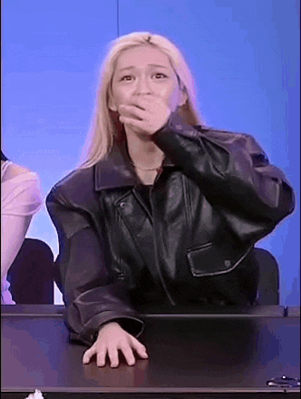 a woman in a leather jacket is sitting at a table covering her mouth .