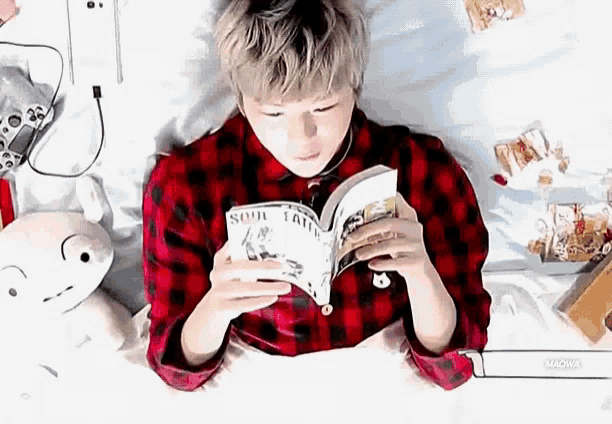 a young man is reading a book while laying on a bed .
