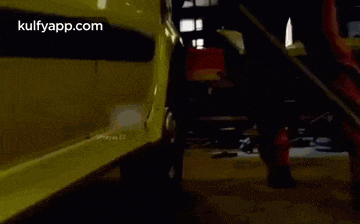 a man in red overalls is walking in front of a yellow car .