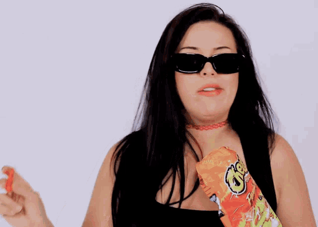 a woman wearing sunglasses and holding a bag of cheetos