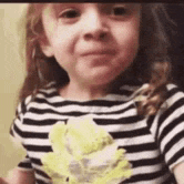 a little girl in a striped shirt is holding a stuffed animal in her hands .
