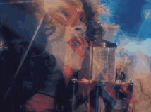a woman is singing into a microphone in a dark room with smoke coming out of her mouth .