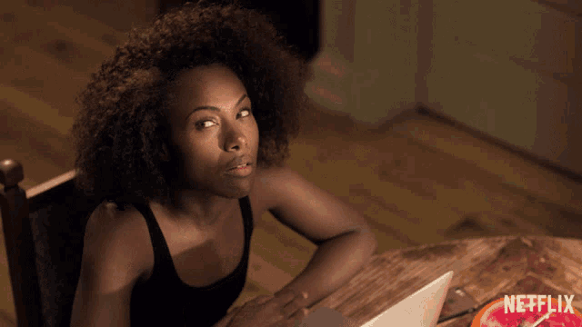 a woman sitting at a table with a laptop and a netflix logo on the bottom right