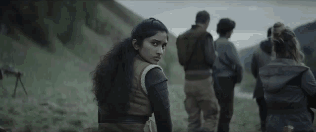 a group of people are standing in a field looking at a woman .