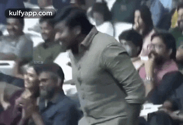 a man is dancing in a crowd of people while sitting in a stadium .