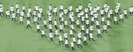 a large group of people in white shirts are standing in a triangle on a field .