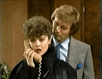 a woman is talking on a telephone while a man looks on .