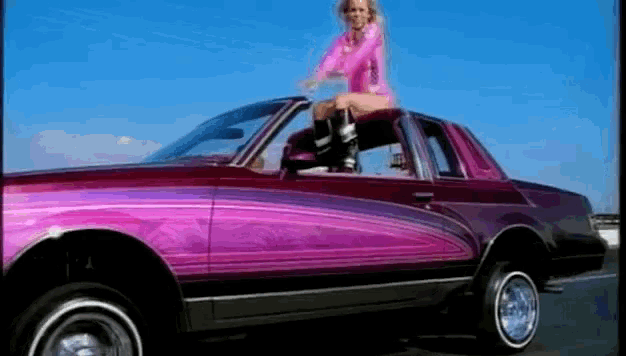 a woman is sitting on the top of a pink car .