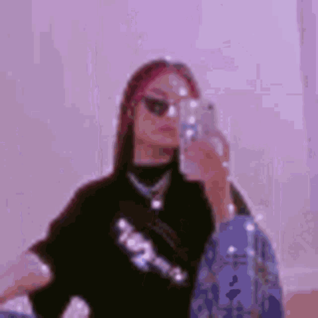 a woman is taking a selfie with her phone in front of a pink wall .
