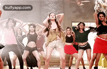 a group of women are dancing together in a room in front of a chandelier .