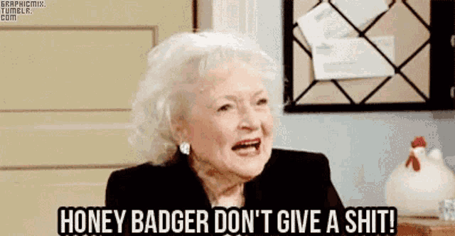 an elderly woman is sitting in front of a bulletin board and saying honey badger do n't give a shit .