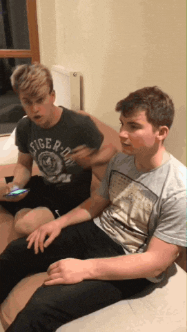 two young men are sitting on a couch one of them is wearing a tiger shirt